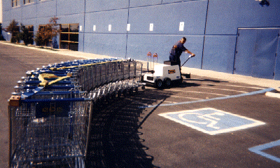 Motorized cart mule moving long line of shopping carts at a retail store. 